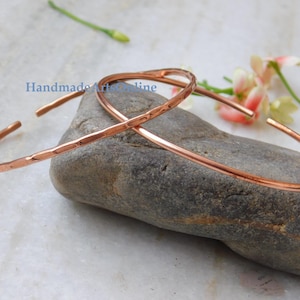 Puede incluir: Dos brazaletes de metal color cobre con un acabado martillado y texturizado. Los brazaletes son abiertos y de forma circular. El texto "HandmadeArtsOnline" es visible en letras azules cerca del centro de la imagen.