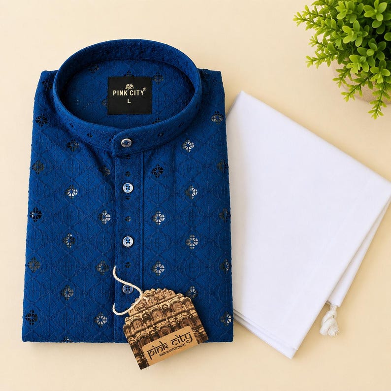 K&ouml;nnte beinhalten: Ein dunkelblaues lang&auml;rmeliges Kurta-Hemd mit Stehkragen, Knopfleiste und einem durchgehenden, lasergeschnittenen geometrischen Muster. Ein wei&szlig;es Stoffst&uuml;ck liegt gefaltet daneben, versehen mit einem angeh&auml;ngten Pink City Markenetikett.