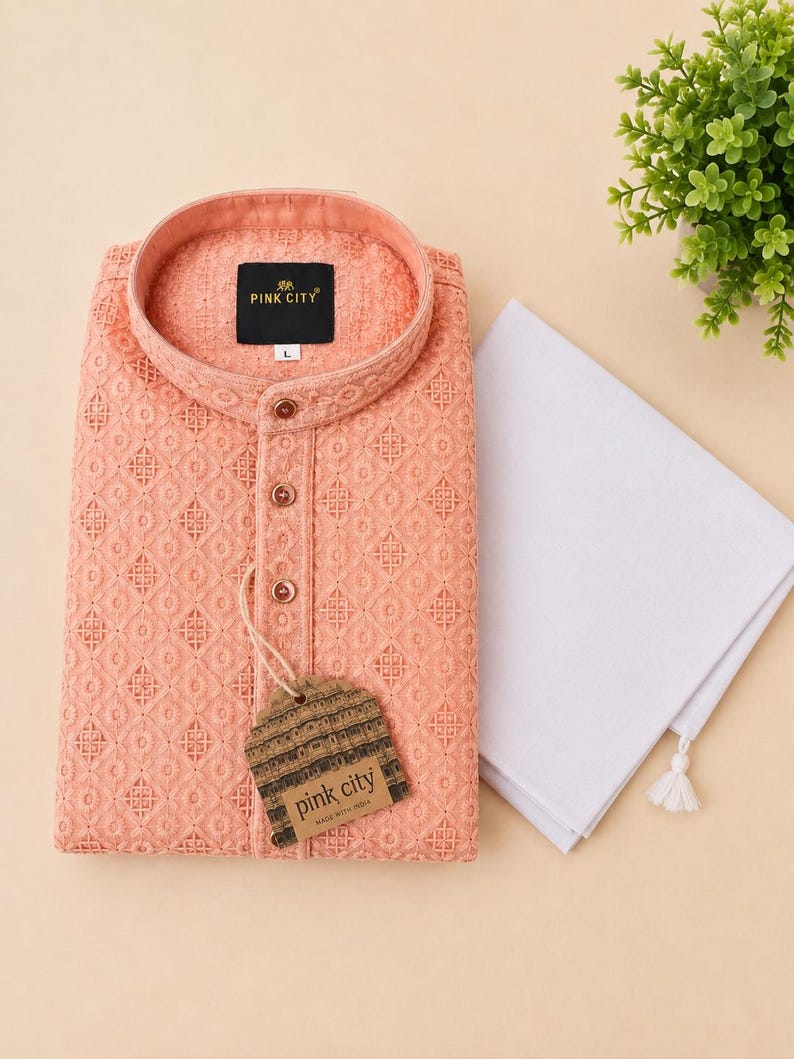K&ouml;nnte beinhalten: Ein pfirsichfarbener Langarm-Kurta mit einem komplizierten gestickten geometrischen Muster, einem Stehkragen und einer Knopfleiste. Ein schwarzes Etikett zeigt PINK CITY mit der Gr&ouml;&szlig;e L. Ein schlichtes, wei&szlig;es, gefaltetes Stoffst&uuml;ck liegt bei.