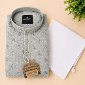 K&ouml;nnte beinhalten: Ein hellgraues, lang&auml;rmeliges Kurta-Hemd mit einem komplizierten, gestickten geometrischen Muster mit kleinen reflektierenden Akzenten, einem Stehkragen und drei Kn&ouml;pfen vorne. Ein wei&szlig;es Stoffst&uuml;ck liegt daneben und ein Etikett zeigt PINK CITY.