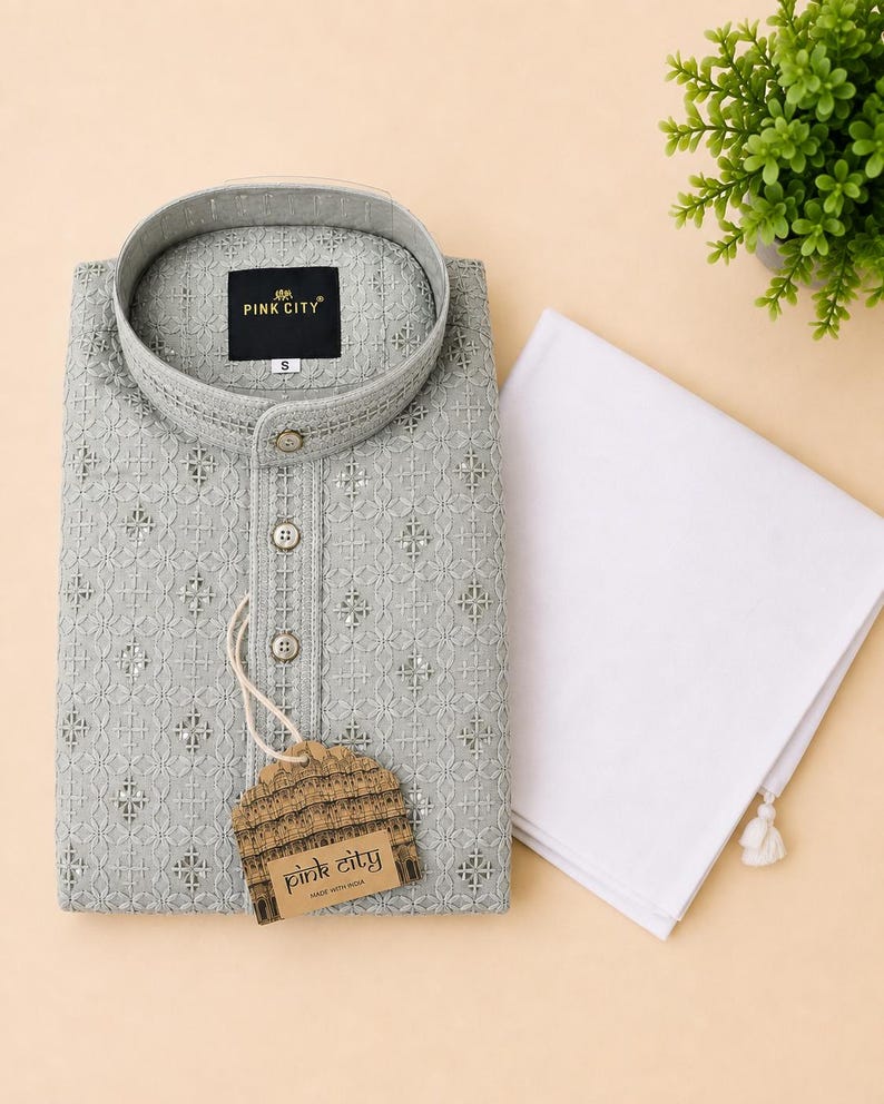 K&ouml;nnte beinhalten: Ein hellgraues, lang&auml;rmeliges Kurta-Hemd mit einem komplizierten, gestickten geometrischen Muster mit kleinen reflektierenden Akzenten, einem Stehkragen und drei Kn&ouml;pfen vorne. Ein wei&szlig;es Stoffst&uuml;ck liegt daneben und ein Etikett zeigt PINK CITY.