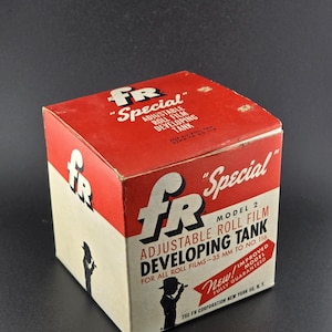 Może przedstawiać: Zabytkowe czerwono-kremowe pudełko na regulowany zbiornik do wywoływania filmu w rolce FR Special Model 2. Pudełko zawiera logo FR, szczegóły produktu i sylwetkę osoby. Tekst brzmi "New! Improved Model Fully Guaranteed."