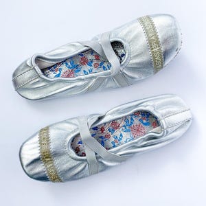 Può includere: Due ballerine argentate con cinturini elastici e solette interne a fantasia floreale. Le ballerine hanno una lucentezza metallica e una fascia con la scritta "R.SONS REPLAY & SONS" sulla parte superiore.