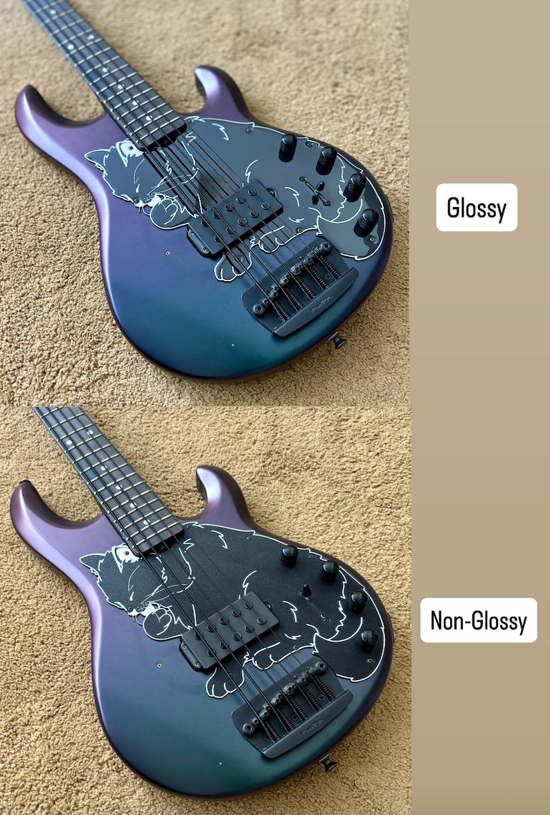 Op de afbeelding: Een basgitaar met een glanzende en niet-glanzende afwerking. De body heeft een verloop van paars naar teal. Een zwarte slagplaat heeft een witte illustratie. De gitaar heeft zwarte hardware en snaren.