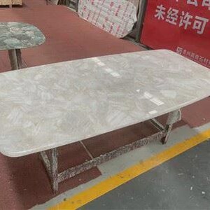 Pu&ograve; includere: Un tavolo rettangolare con una superficie chiara e decorata. Il tavolo ha una base grigio chiaro ed &egrave; posto su una superficie rossa con una striscia gialla. Un altro tavolo con una superficie verde &egrave; visibile sullo sfondo.