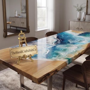 May include: A rectangular dining table with a natural wood edge and a glossy resin inlay featuring blue, turquoise, and white swirling ocean wave patterns. A gold ornate easel holds a rectangular sign reading TheHandiCraftsHubCo.
