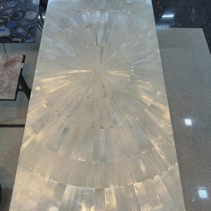 May include: A rectangular, white table with a radial design on the surface. The table's surface is made of rectangular pieces arranged in concentric circles, creating a sunburst effect. The table is set on a light-colored floor.