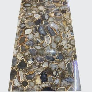 May include: A rectangular stone slab with a mosaic pattern of irregularly shaped, polished agate stones in shades of gray, brown, and cream. The stones are tightly fitted together, creating a unique and textured surface. The edges are smooth and polished.