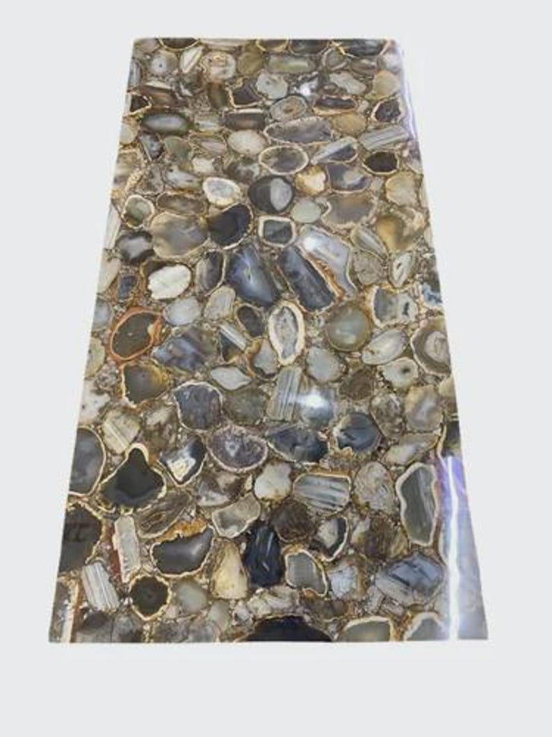 May include: A rectangular stone slab with a mosaic pattern of irregularly shaped, polished agate stones in shades of gray, brown, and cream. The stones are tightly fitted together, creating a unique and textured surface. The edges are smooth and polished.