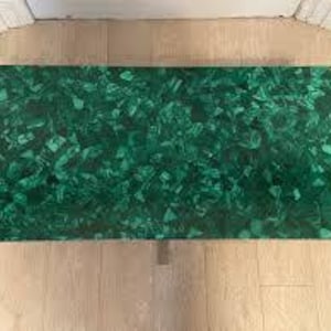 Puede incluir: Mesa de centro rectangular de malaquita verde. La mesa tiene una superficie pulida con un patrón arremolinado de tonos verdes oscuros y claros. La mesa mide aproximadamente 122 cm de largo y 61 cm de ancho.