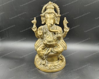 May include: A golden-colored statue of the Hindu deity Ganesha, seated in a cross-legged pose. The statue features intricate details, including a large head with elephant features, multiple arms, and ornate jewelry. The figure is on a decorative base.