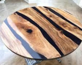 May include: A round table featuring a natural wood grain surface with prominent knots and light brown tones, intersected by three distinct, smooth, black resin inlays that run diagonally across the circular tabletop, supported by a metal base.