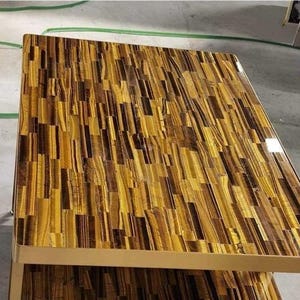 May include: A rectangular coffee table with a unique surface made of tiger eye stone. The tabletop features a mosaic pattern of golden yellow and brown tones. The table has a gold-colored metal frame.