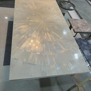 Op de afbeelding: Een rechthoekige, witte kwartstafel met een radiaal ontwerp. Het oppervlak van de tafel is gemaakt van rechthoekige kwartsstukken die in een zonnestraalpatroon zijn gerangschikt. De tafel staat op een lichtgekleurde vloer.