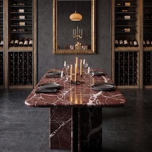 May include: A dining room scene featuring a rectangular marble table with a red and white veined pattern. The table is set with black plates, wine glasses, and lit candles. A gold-framed mirror hangs on the wall, reflecting the room.