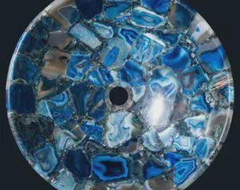Pode incluir: Bacia de lavatório redonda, estilo mosaico, com acabamento polido. A bacia é feita de pedaços irregulares de pedra azul, branca e cinza, criando um padrão único. Um orifício de drenagem central é visível. Projetada para uso em banheiro.