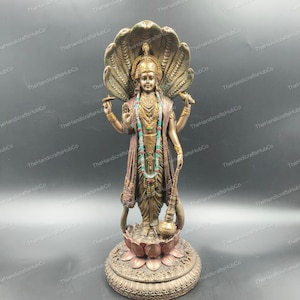 May include: A bronze-colored statue of a deity, adorned with intricate details. The figure stands on a lotus flower base, with a multi-headed serpent forming a halo behind the head. The statue features ornate jewelry and holds symbolic objects.