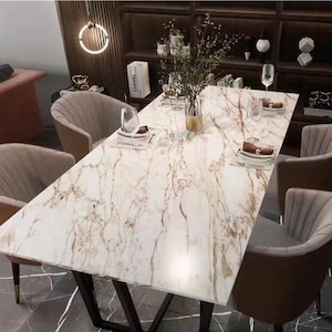 Puede incluir: Una mesa de comedor rectangular con superficie efecto mármol y patas oscuras. La mesa está rodeada de seis sillas tapizadas. La habitación tiene un diseño moderno con un mueble de madera oscura y objetos decorativos.