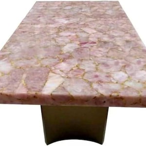 May include: A rectangular table with a pink quartz top. The surface is made of irregular, interlocking pieces with gold-colored veins. The table has a solid, brown base.