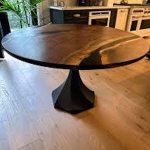 May include: A round, dark brown wooden table with a black pedestal base. The table has a diameter of approximately 48 inches. The tabletop features a unique design with a lighter-colored, river-like inlay. The table is in a well-lit room with hardwood floors.