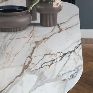 May include: A close-up of a marble-patterned table with brown and black veining. Three brown vases with pink flowers sit on the table. The vases have a ribbed texture and varying shapes, adding visual interest to the scene.