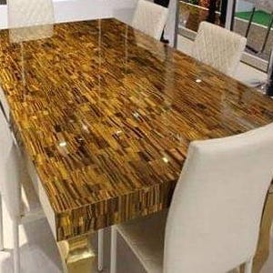 May include: A rectangular dining table with a glossy, patterned surface in shades of brown and gold. The table is surrounded by white upholstered chairs with gold accents on the legs. The table's surface has a unique, textured appearance.