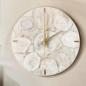 Pode incluir: Relógio de parede redondo com um mostrador branco em estilo mosaico e ponteiros e marcadores dourados. O mostrador do relógio é feito de peças de formato irregular, criando uma textura única. O relógio está montado em uma parede clara.
