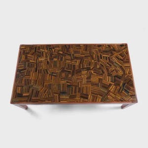 May include: Rectangular coffee table with a mosaic top made of tiger's eye gemstones. The table has a dark brown wooden frame and legs. The mosaic top features a pattern of brown, gold, and black stone pieces.