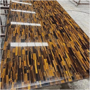 May include: A large, rectangular countertop with a mosaic pattern of tiger's eye stone. The surface is a mix of golden-brown and dark brown tones, with a polished, reflective finish. The stone pieces are arranged in a vertical, linear design.