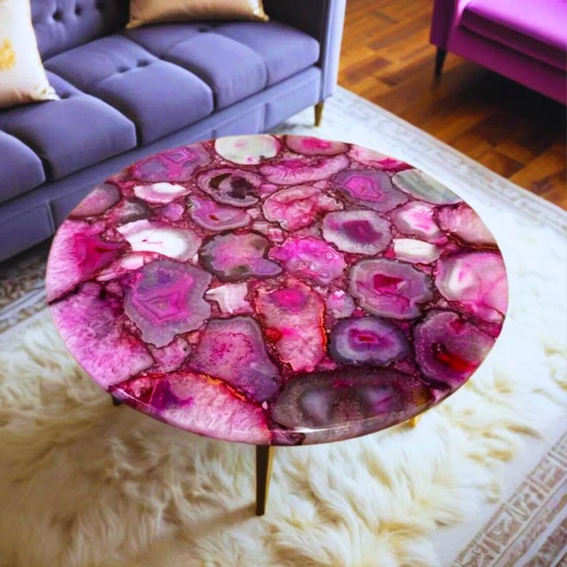 May include: A round coffee table featuring a tabletop composed of numerous polished, vibrant pink and magenta agate slices. The surface displays a mosaic of translucent, crystalline patterns in varying shades of fuchsia, white, and deep purple, supported by thin, metallic legs.