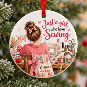 May include: A round white ceramic ornament featuring an illustration of a person with a bun hairstyle sitting at a desk with a sewing machine, a cat, and sewing supplies. The text reads Just a girl who love Sewing and the name Emma.