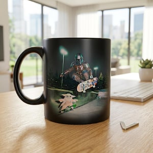 May include: Black ceramic mug featuring a graphic of a Mandalorian character skateboarding. The design includes a green-lit skate park scene with a Grogu character on a skateboard. The mug has a black handle and a glossy finish.