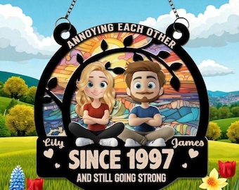 May include: A black metal sign with the text "ANNOYING EACH OTHER" and "SINCE 1997 AND STILL GOING STRONG". The sign features a cartoon couple and is decorated with flowers and a colorful background.