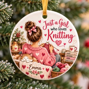 May include: A round white ceramic ornament featuring a person with a brown bun hairstyle and a pink heart-patterned sweater knitting. The text reads Just a Girl who loves Knitting and Emma. A sleeping orange cat, yarn balls, and books are visible.
