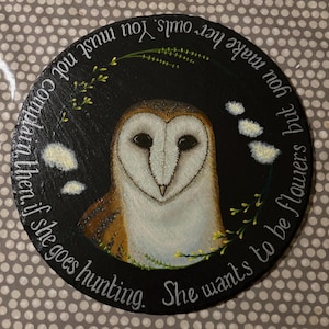 Könnte beinhalten: Runde, schwarze Schiefer-Kunst mit einer detaillierten Malerei einer Schleiereule. Die Eule hat ein weißes Gesicht und braune und beige Federn. Das Kunstwerk enthält weißen Text und florale Akzente.