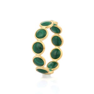 Puede incluir: Un anillo dorado con una serie de piedras ovaladas de malaquita verde oscuro. Cada piedra está engastada en un bisel dorado, creando un patrón continuo. El anillo se muestra sobre un fondo blanco.