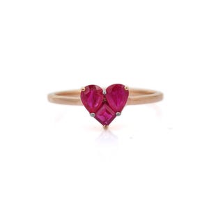 May include: A gold ring with a heart-shaped design. The heart is made of three vibrant red gemstones: two pear-shaped stones and one square-cut stone. The ring's band is a delicate gold colour.