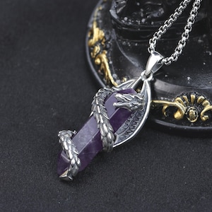 May include: A silver pendant necklace with a purple crystal, encircled by a detailed dragon. The dragon's head and tail are visible, and the crystal is rectangular. The chain is a silver curb chain.