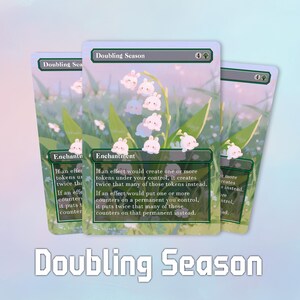 Könnte beinhalten: Drei Doubling Season-Karten mit einem Blumen- und Hasenmuster. Die Karten haben einen grünen Rand und den Text "Doubling Season" oben und "Enchantment" unten. Die Karten haben einen hellblauen Hintergrund mit dem Text "Doubling Season" unten.