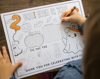 Op de afbeelding: Een Halloween kleurplaat met de tekst "BOO! EVER IS TWO!" en "THANK YOU FOR CELEBRATING WITH US." Bevat een woordzoeker, boter-kaas-en-eieren en Halloween-illustraties. Een kind kleurt de pagina met een oranje kleurpotlood.