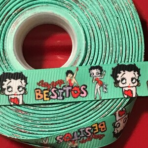 May include: A roll of green ribbon with a repeating pattern of cartoon characters and the word "Besitos".