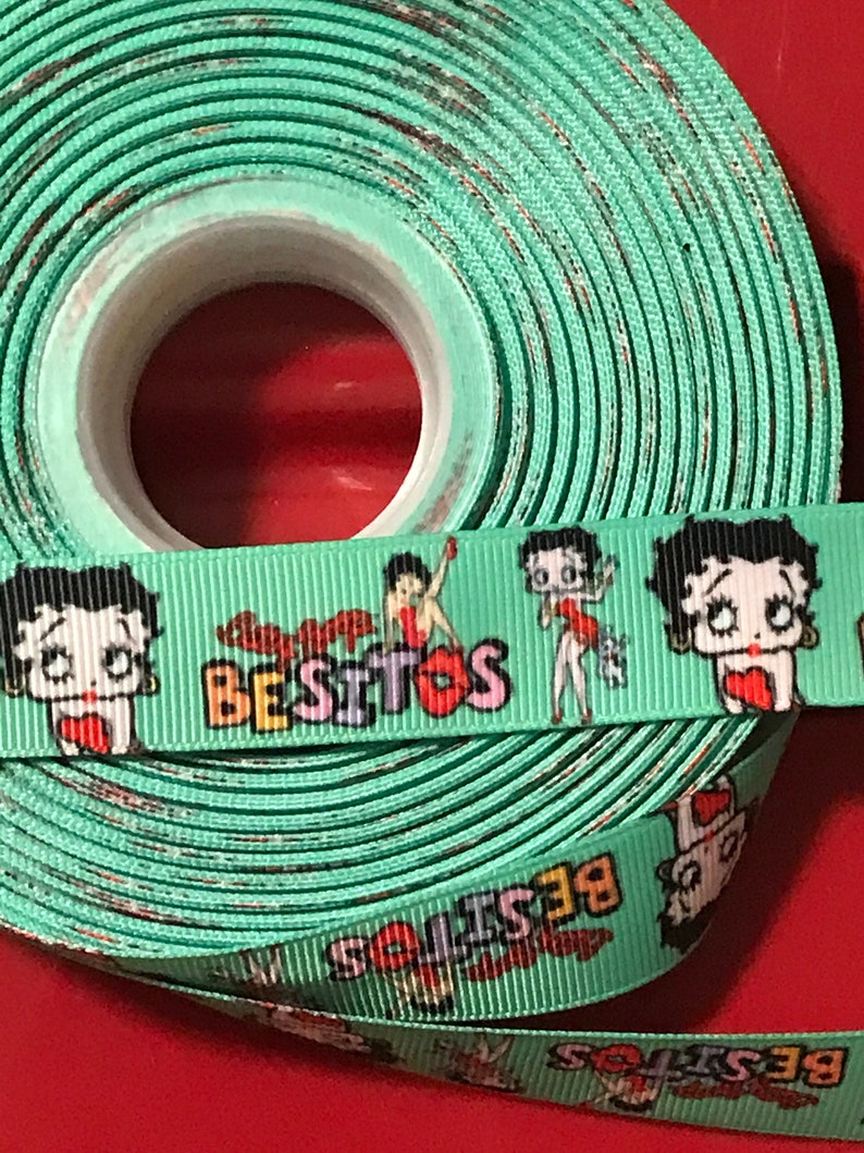 May include: A roll of green ribbon with a repeating pattern of cartoon characters and the word "Besitos".