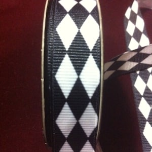 Op de afbeelding: Een rol zwart-witte ruitjesband. Het lint zit op een spoel en is klaar om te gebruiken voor knutselen of decoreren.