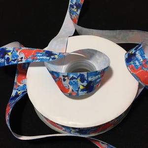Peut inclure: Un rouleau de ruban bleu et blanc avec un motif répété de Dory et d'autres personnages de Finding Nemo. Le ruban mesure 2,5 cm de large et est parfait pour l'artisanat, les cadeaux et la décoration.