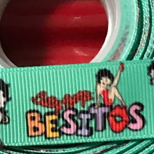 May include: Green ribbon with a cartoon character and the text "Super Besitos" in colorful letters.