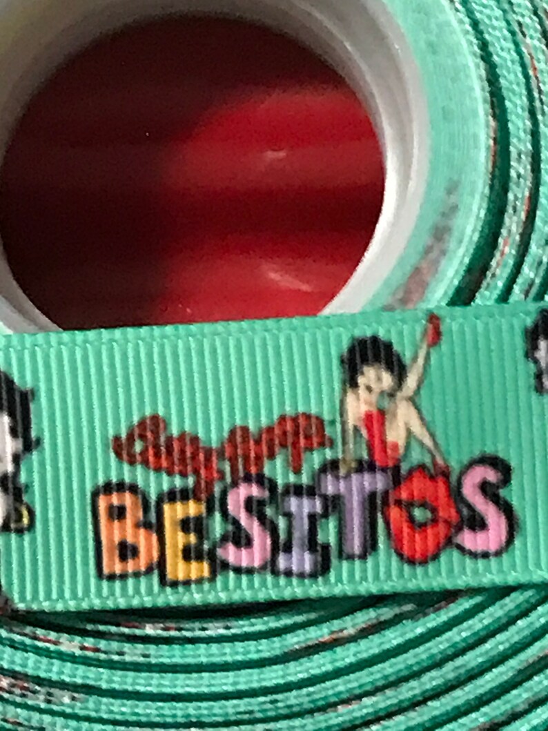 May include: Green ribbon with a cartoon character and the text "Super Besitos" in colorful letters.