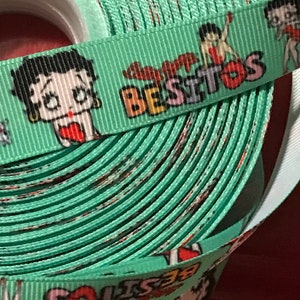 May include: A green ribbon with a repeating pattern of a cartoon character with the text "Super Besitos" printed on it.