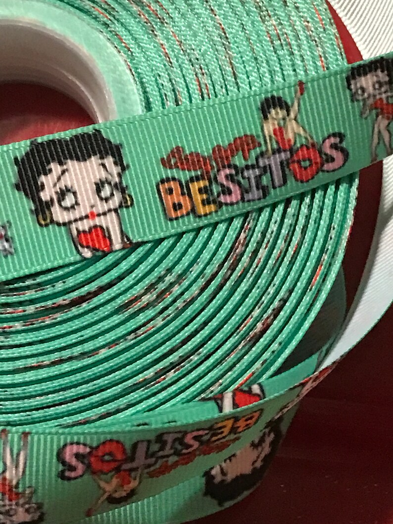 May include: A green ribbon with a repeating pattern of a cartoon character with the text "Super Besitos" printed on it.