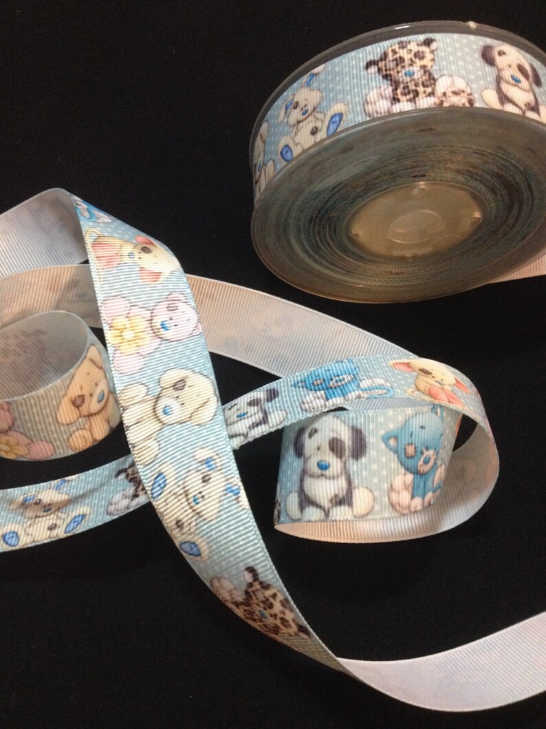 May include: A roll of blue ribbon with a white background and a repeating pattern of cartoon dogs and cats. The ribbon is on a black surface.