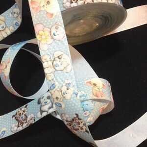 May include: A blue ribbon with a white polka dot pattern and a repeating design of teddy bears and a leopard print animal. The ribbon is rolled up on a spool.
